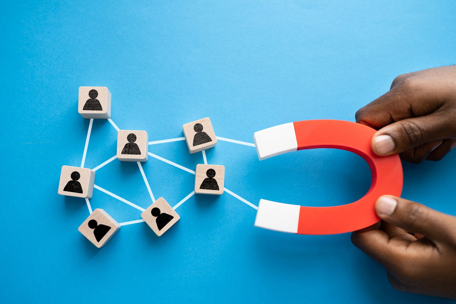 Mano sosteniendo un imán atrae bloques con iconos de personas, simbolizando la atracción de clientes en marketing.