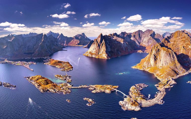 Vista aérea de islas Lofoten, Noruega, con montañas y mar bajo un cielo despejado y soleado.