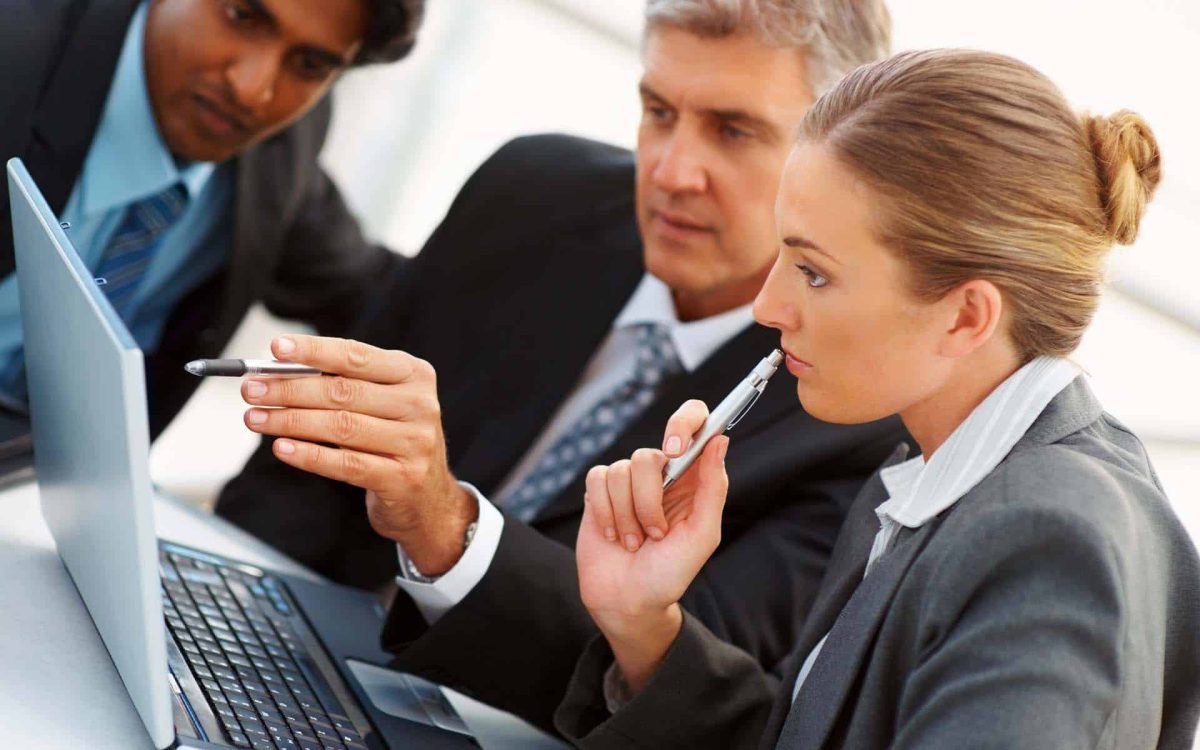 Tres profesionales revisan información en una computadora portátil, discutiendo estrategias y tomando notas.