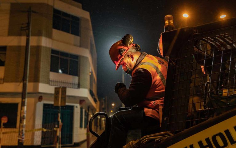 Trabajador de construcción en la noche, ajustándose el equipo de seguridad en un entorno urbano iluminado.