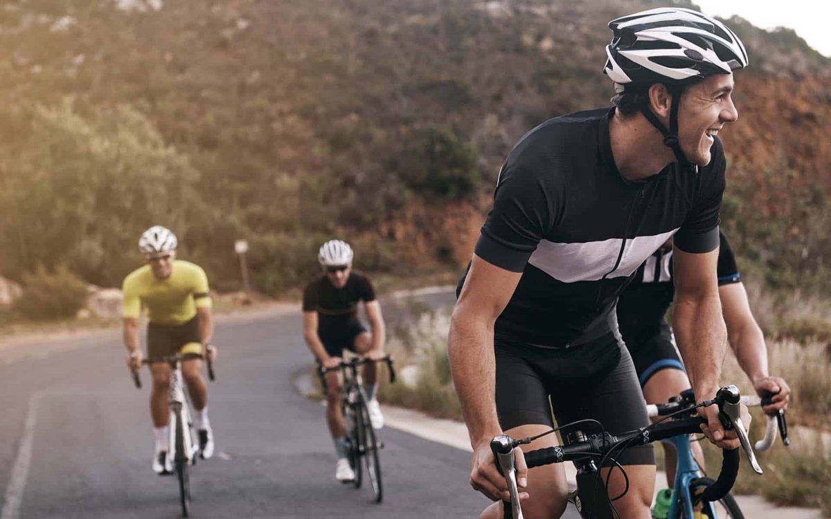 Ciclistas disfrutando de una ruta montañosa, sonriendo mientras pedalean en un entorno natural y soleado.