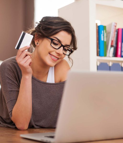 Mujer sonriente utilizando una tarjeta de crédito mientras compra en línea desde su computadora portátil en casa.