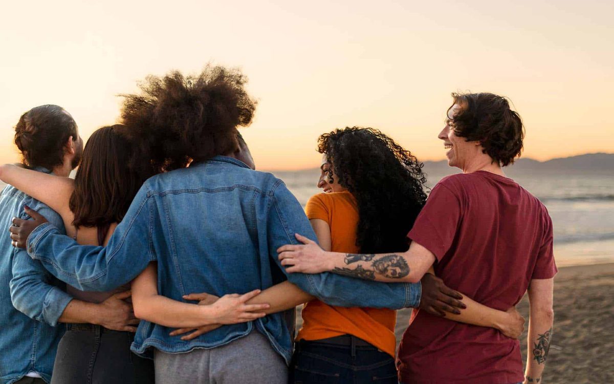 Grupo de amigos abrazados, contemplando el atardecer en la playa, transmitiendo alegría y conexión emocional.
