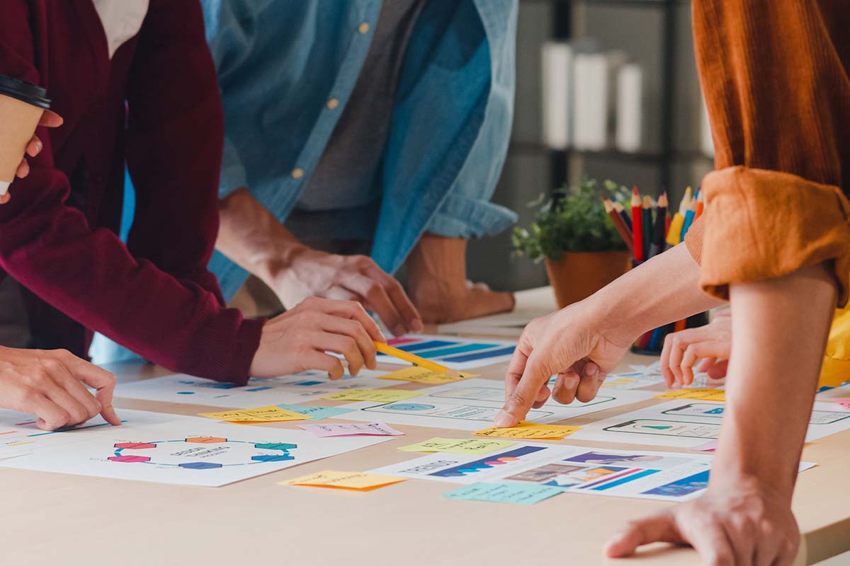 Grupo de personas colaborando en un proyecto creativo, analizando gráficos y notas en una mesa de trabajo.