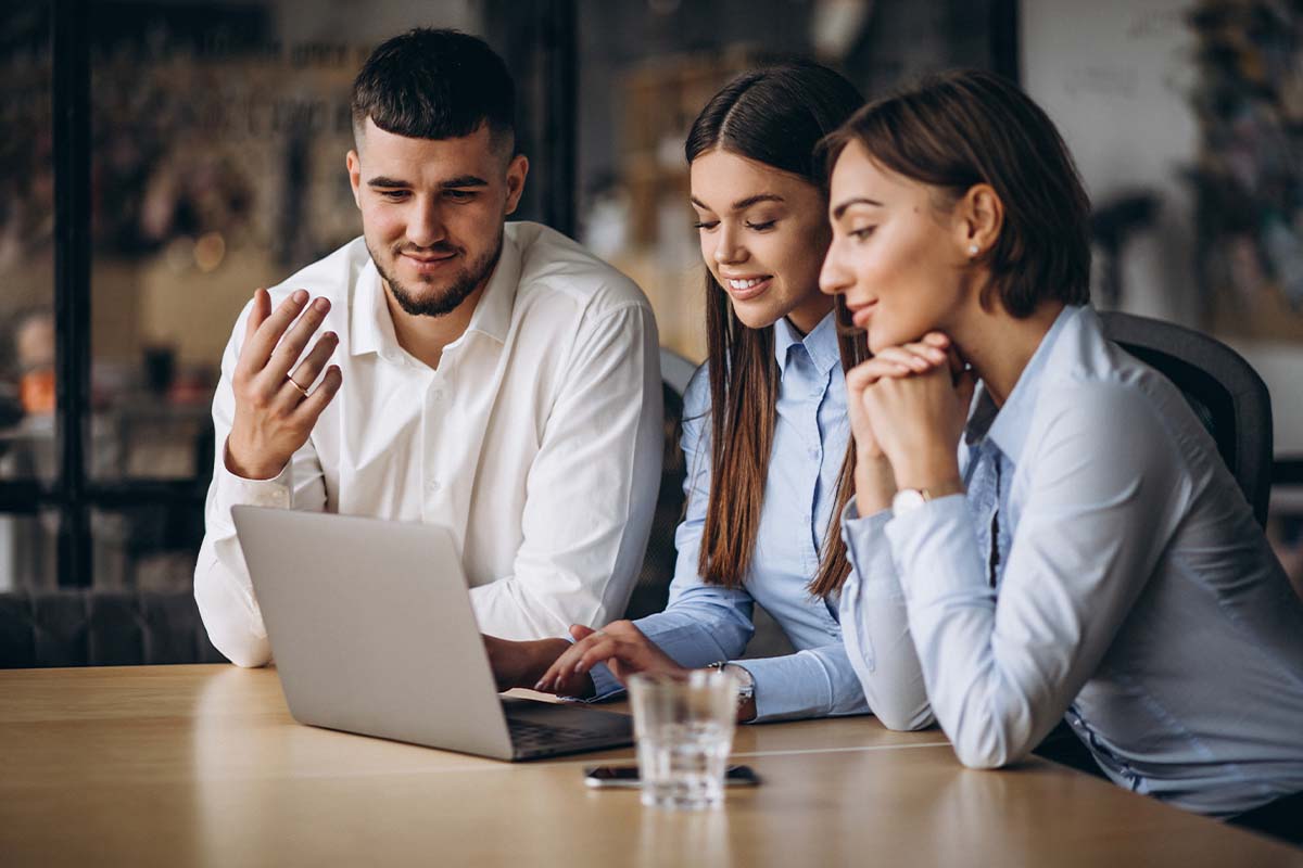 Tres profesionales discuten ideas frente a una laptop en una oficina moderna, mostrando interés y colaboración.