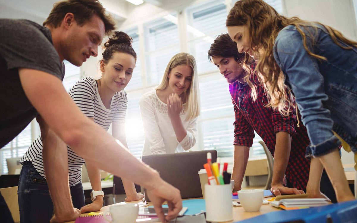 Grupo de personas colaborando en una mesa, analizando ideas y trabajando en un proyecto creativo.
