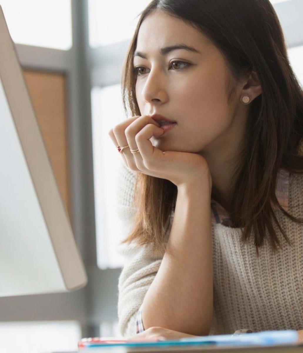 Mujer pensativa frente a la computadora, reflexionando sobre ideas en un ambiente luminoso y acogedor.