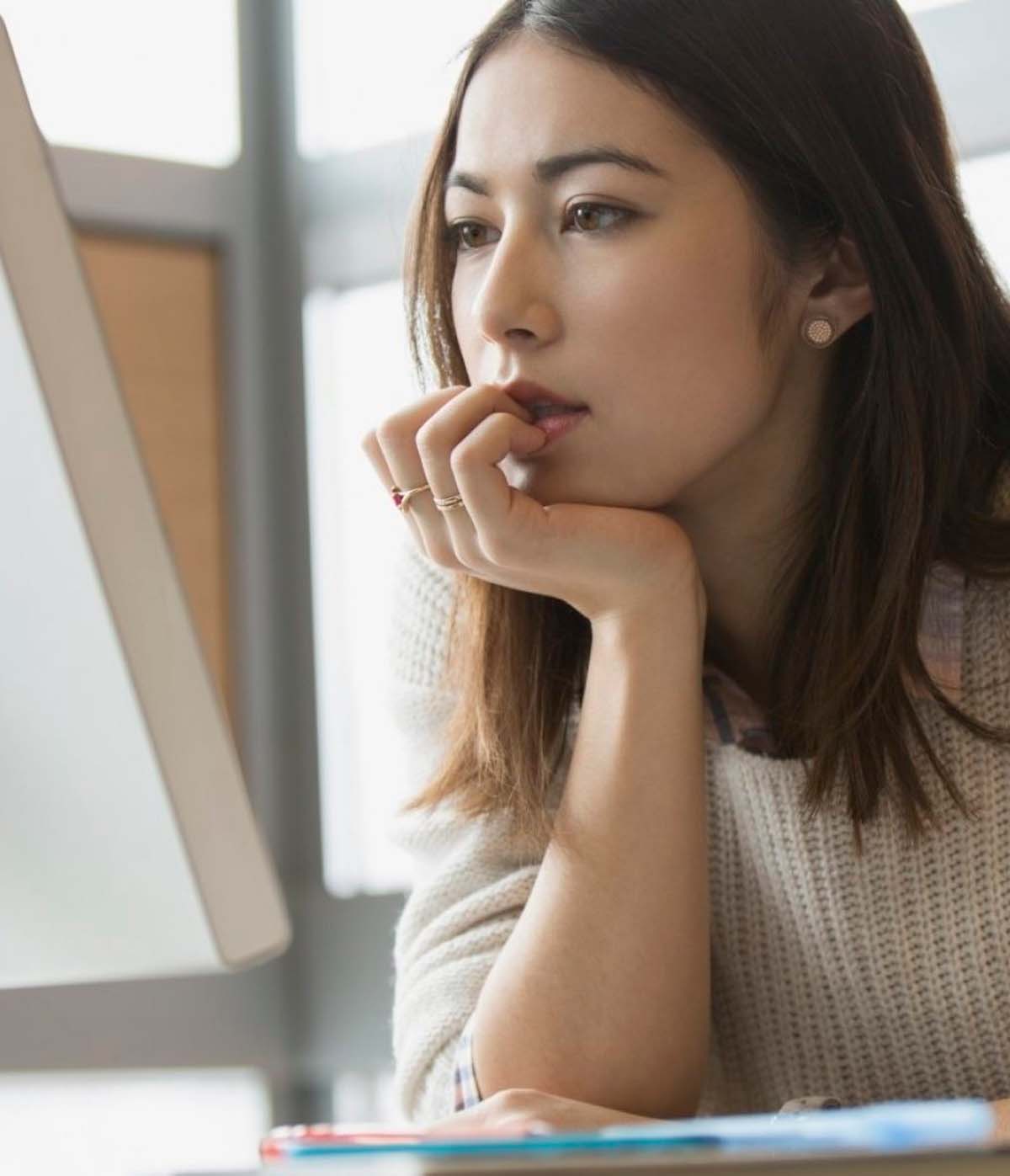 Mujer pensativa frente a la computadora, reflexionando sobre ideas en un ambiente luminoso y acogedor.