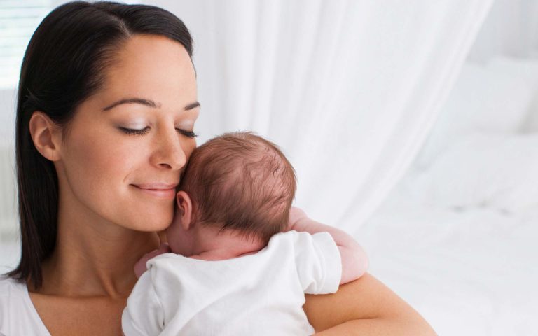 Mujer abraza a su bebé en un ambiente tierno y cálido, mostrando amor y conexión maternal.