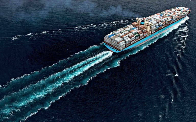 Buque portacontenedores navegando por el océano, dejando estelas de espuma en las aguas profundas del mar.