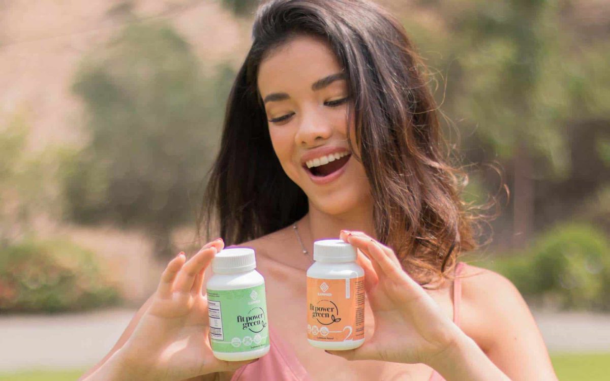 Joven sonriente sostiene frascos de suplementos naturales en un entorno al aire libre, destacando su bienestar.