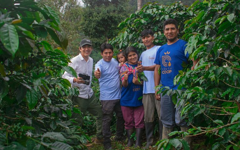 Grupo de personas sonriendo en un cafetal, mostrando su trabajo en la agricultura y la cultura del café.